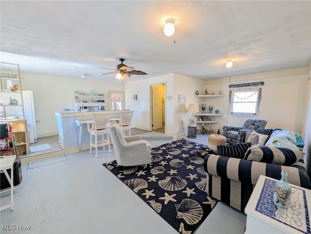 living area featuring baseboards, concrete floors, and ceiling fan