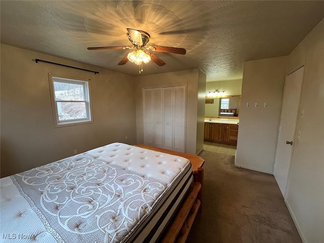 bedroom with baseboards, ensuite bath, light carpet, a closet, and a textured ceiling