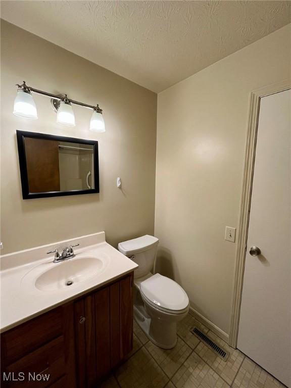 half bath with visible vents, toilet, vanity, and a textured ceiling