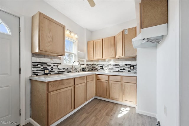 kitchen with light brown cabinetry, under cabinet range hood, light wood-type flooring, light countertops, and decorative backsplash