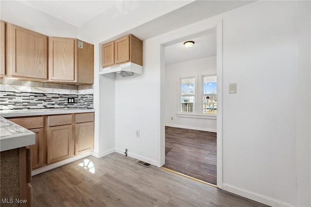 kitchen with wood finished floors, light brown cabinets, decorative backsplash, light countertops, and under cabinet range hood