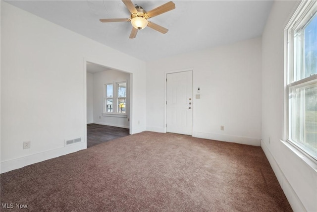 unfurnished room featuring carpet flooring, a ceiling fan, visible vents, and a wealth of natural light