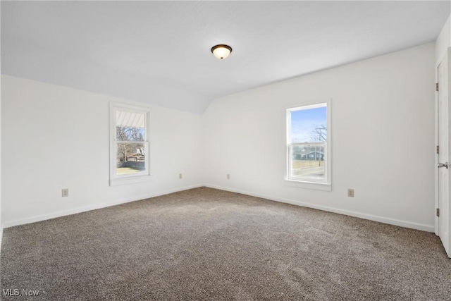 carpeted spare room featuring baseboards and vaulted ceiling