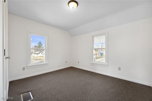 unfurnished room with vaulted ceiling, baseboards, visible vents, and dark colored carpet