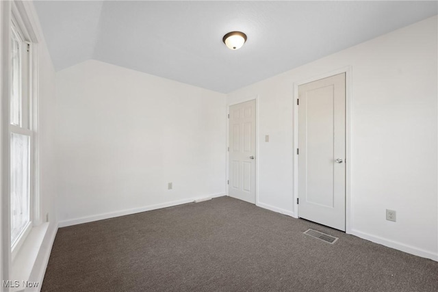 unfurnished bedroom with visible vents, dark carpet, baseboards, and vaulted ceiling