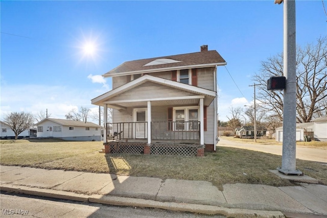 view of front of property featuring a chimney, covered porch, a shingled roof, and a front lawn