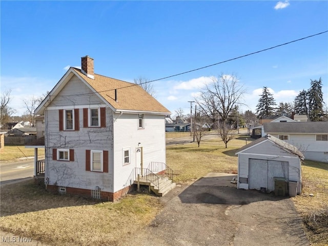 view of side of home with a detached garage, a shed, a chimney, a yard, and an outdoor structure