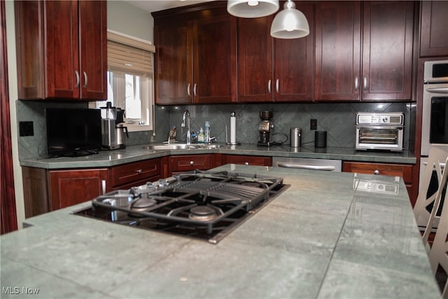 kitchen with a sink, black gas cooktop, backsplash, double oven, and hanging light fixtures