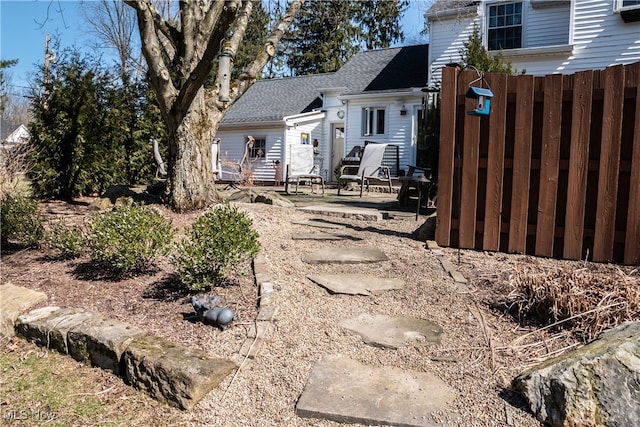 exterior space with fence, a shingled roof, and a patio area