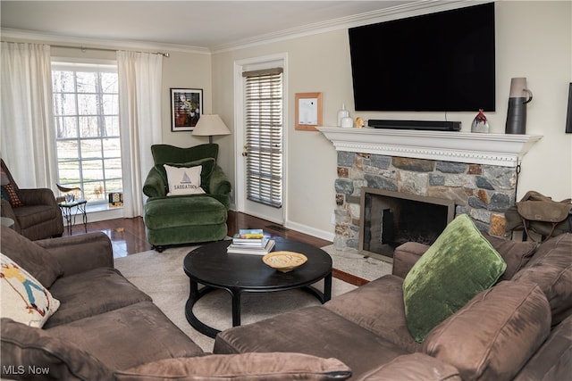 living room with baseboards, wood finished floors, a stone fireplace, and ornamental molding