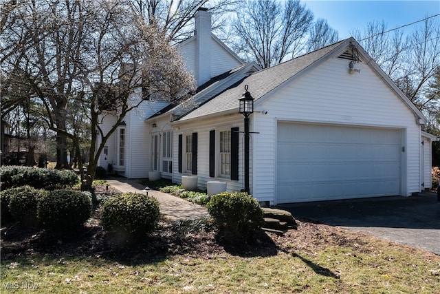 view of side of home featuring a garage, a shingled roof, a chimney, and aphalt driveway