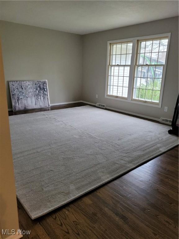 unfurnished room with visible vents, baseboards, and dark wood-type flooring