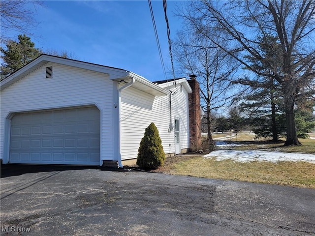 view of property exterior with aphalt driveway, a chimney, and a garage