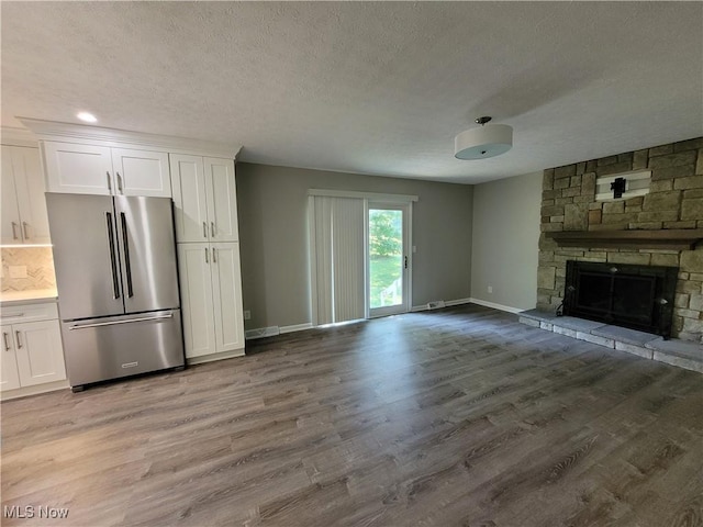 unfurnished living room with a stone fireplace, light wood-style flooring, baseboards, and a textured ceiling