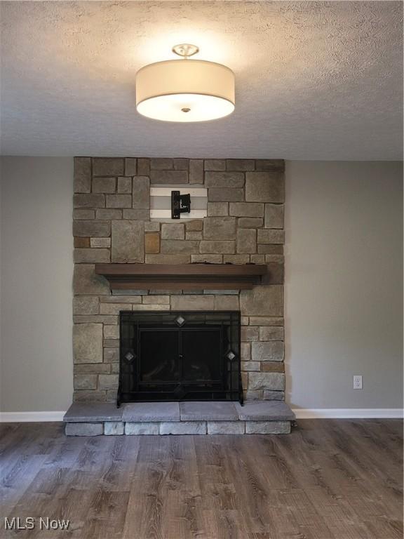 details with a stone fireplace, a textured ceiling, baseboards, and wood finished floors