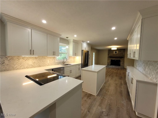 kitchen with a sink, a kitchen island, stovetop, high quality fridge, and dark wood-style flooring