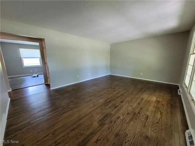 empty room featuring visible vents, baseboards, and dark wood-style flooring