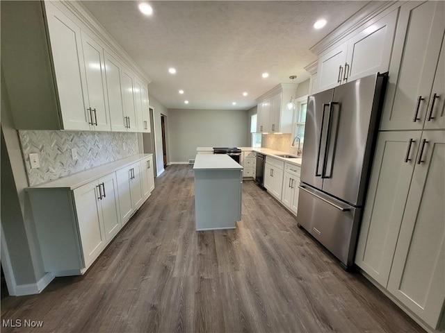 kitchen with a sink, a kitchen island, dark wood finished floors, stainless steel appliances, and light countertops