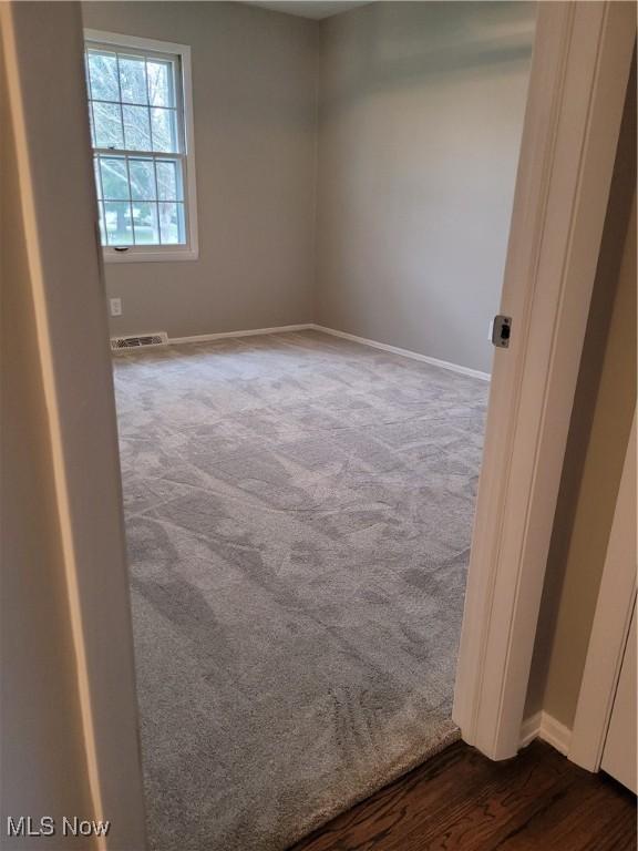 spare room featuring visible vents, dark carpet, and baseboards