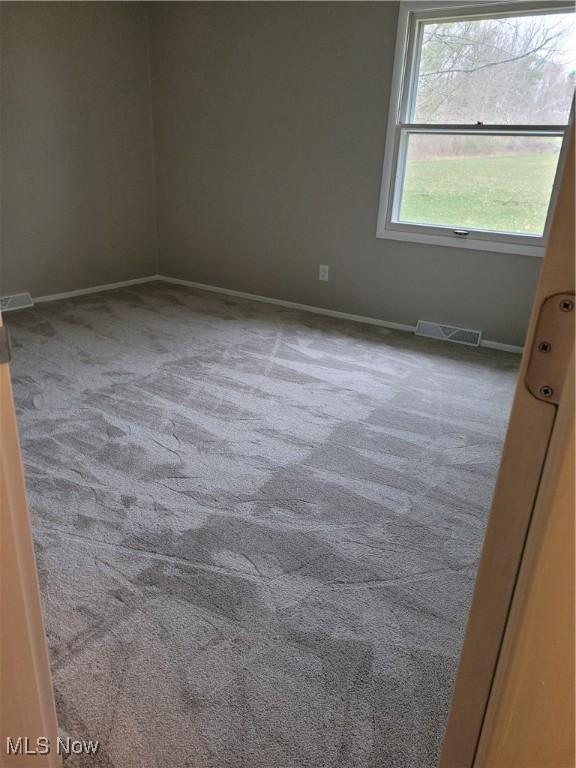 carpeted spare room featuring visible vents and baseboards