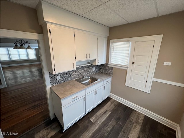 kitchen with a sink, dark wood finished floors, white cabinets, decorative backsplash, and baseboards