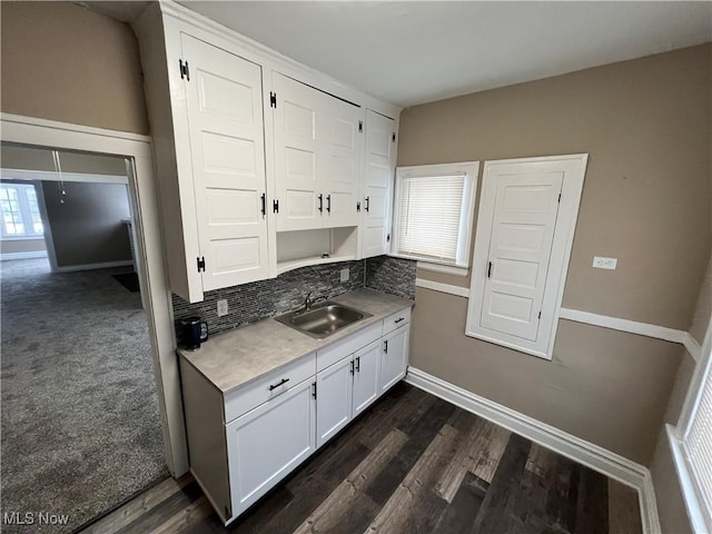 kitchen featuring a sink, dark wood-style floors, white cabinetry, light countertops, and baseboards