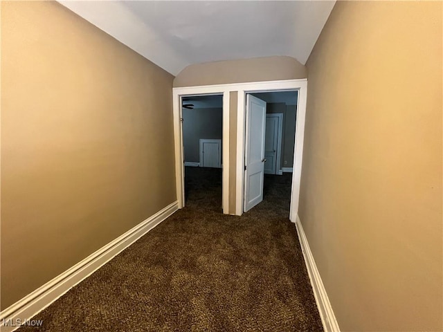 corridor featuring dark carpet, baseboards, and lofted ceiling