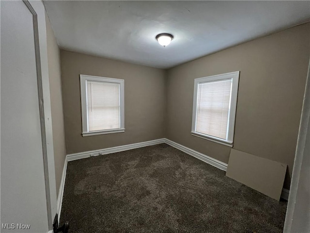 empty room featuring baseboards and dark colored carpet