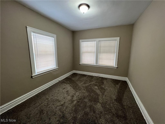 unfurnished room featuring baseboards and dark carpet