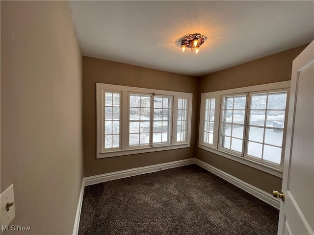 spare room featuring baseboards and dark carpet