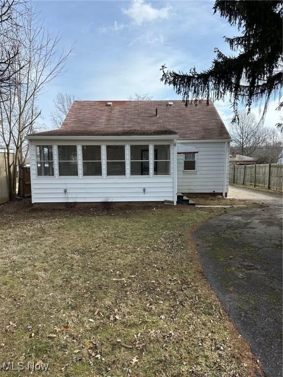 back of property with aphalt driveway, a yard, and fence