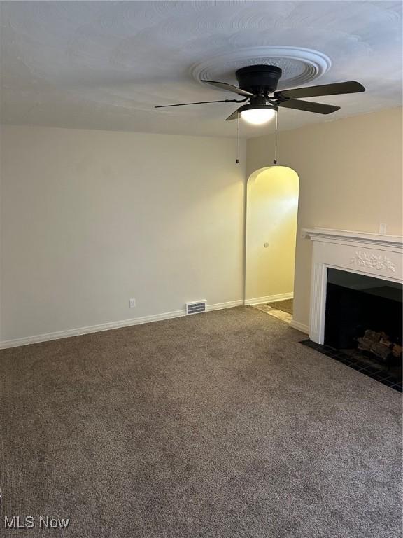 unfurnished living room with baseboards, visible vents, carpet floors, a fireplace with flush hearth, and ceiling fan