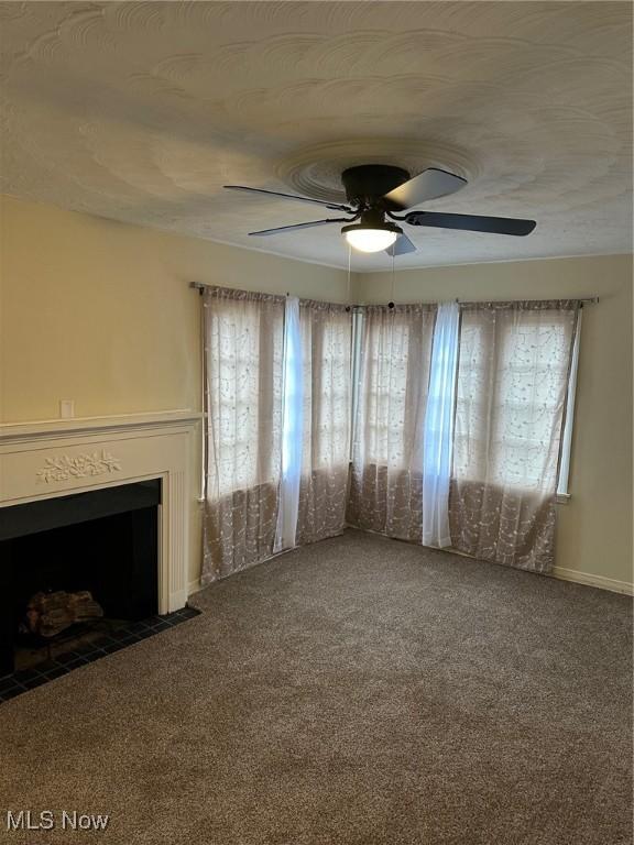 unfurnished living room with a fireplace with flush hearth, ceiling fan, and carpet