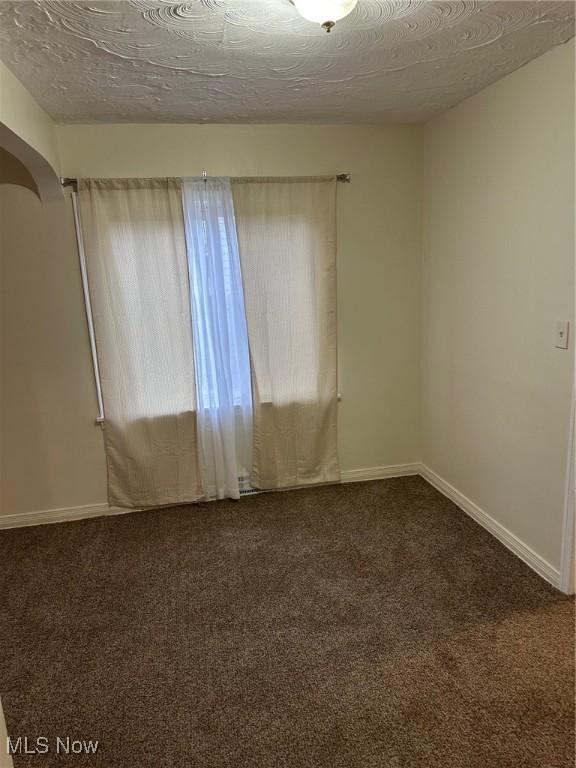 carpeted spare room featuring arched walkways, a textured ceiling, and baseboards