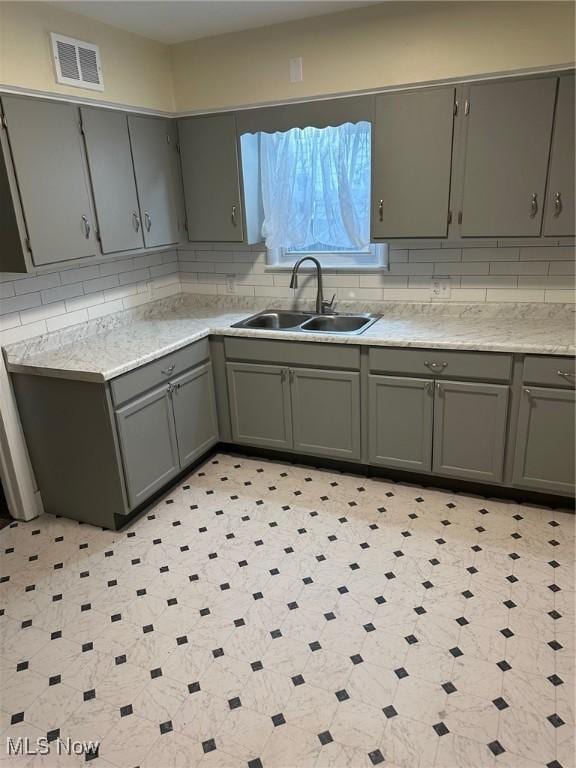 kitchen with visible vents, backsplash, gray cabinetry, and a sink