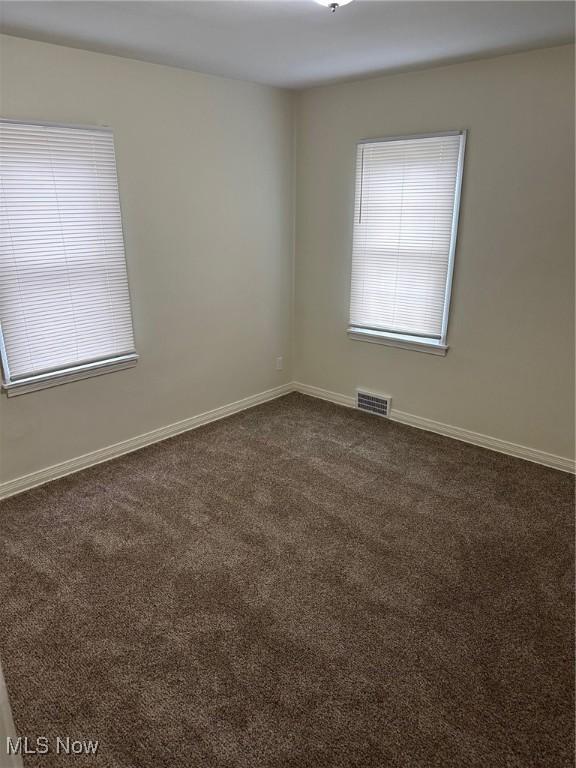 empty room with visible vents, baseboards, and dark carpet