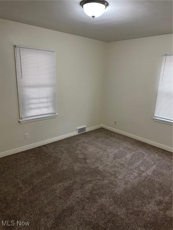 empty room with baseboards, visible vents, and dark colored carpet