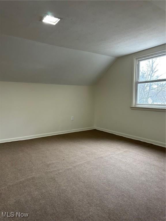 additional living space featuring lofted ceiling, baseboards, and dark colored carpet