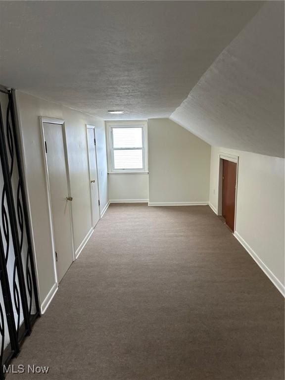 bonus room with vaulted ceiling, a textured ceiling, baseboards, and dark colored carpet