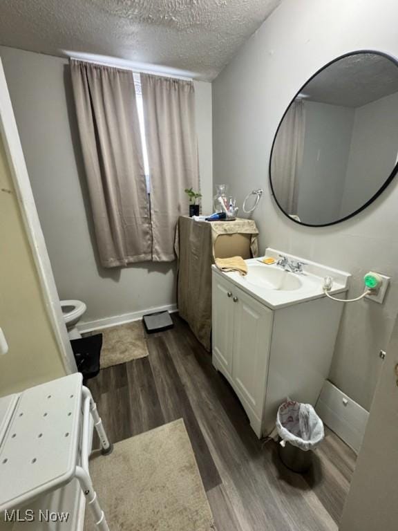 half bathroom featuring toilet, a textured ceiling, wood finished floors, baseboards, and vanity