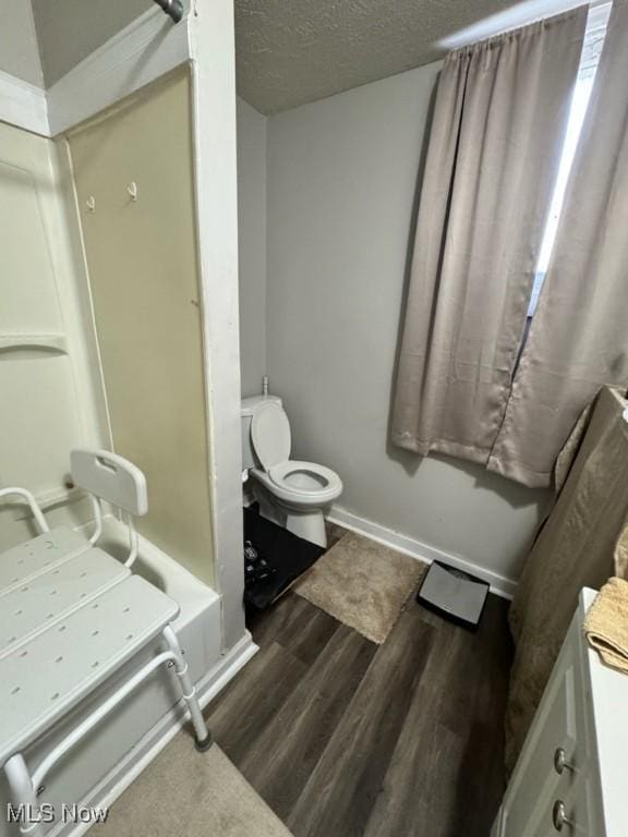 full bathroom featuring toilet, a tub to relax in, a textured ceiling, wood finished floors, and baseboards