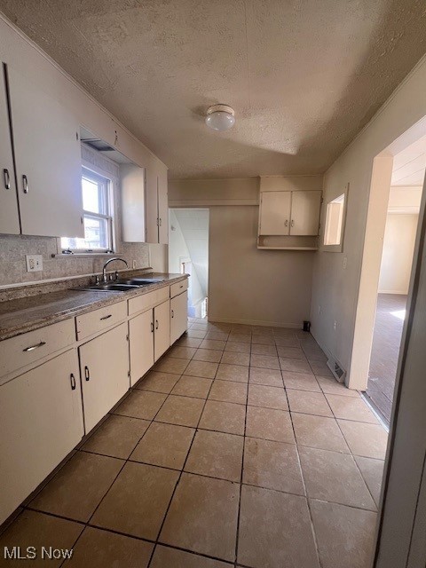 kitchen with a sink, a textured ceiling, white cabinets, light tile patterned floors, and decorative backsplash