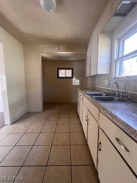 kitchen with white cabinets, light tile patterned floors, backsplash, and a sink