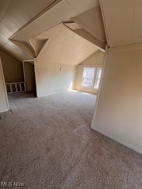 bonus room featuring a decorative wall, vaulted ceiling with beams, and carpet