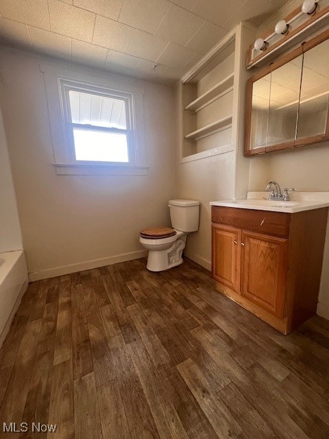 bathroom with vanity, wood finished floors, baseboards, a bathing tub, and toilet