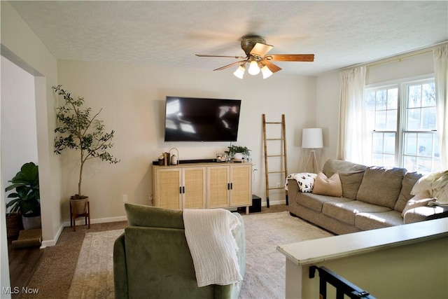 living room featuring ceiling fan, light colored carpet, baseboards, and a textured ceiling