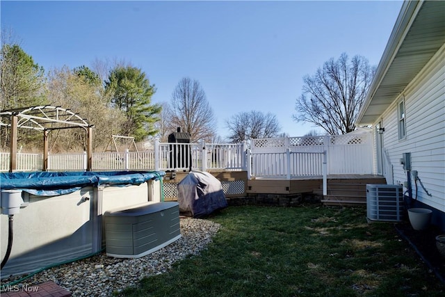 view of yard with a covered pool, a deck, central AC, and fence