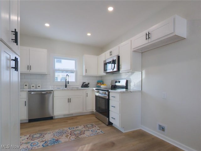 kitchen with backsplash, white cabinetry, stainless steel appliances, and a sink