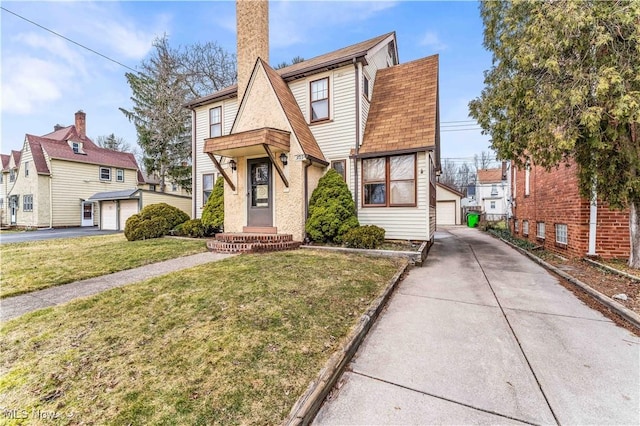 tudor home with a detached garage, an outbuilding, roof with shingles, and a front lawn