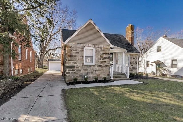 view of front facade with a front yard, roof with shingles, a chimney, an outbuilding, and stone siding